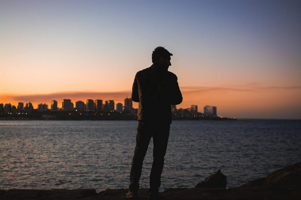 A man standing on the shore of a body of water at sunset