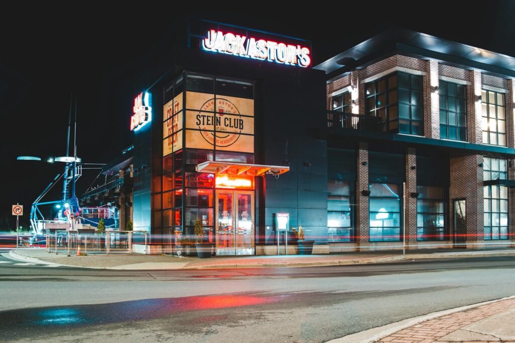 Exterior of modern building with glass facade and illuminated signboard located near asphalt roadway at night