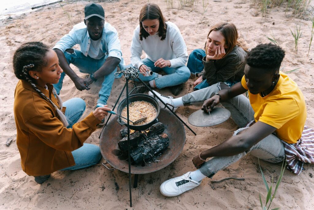 People Sitting on Sand While Cooking Food