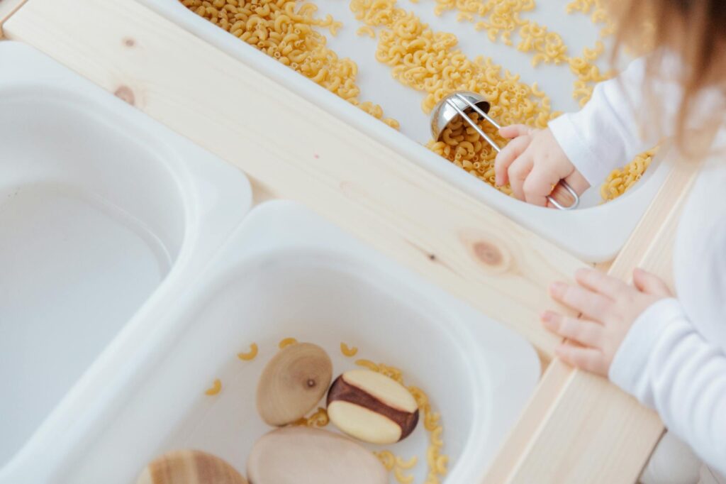 Little girl collect raw pasta with metal spoon in plastic container