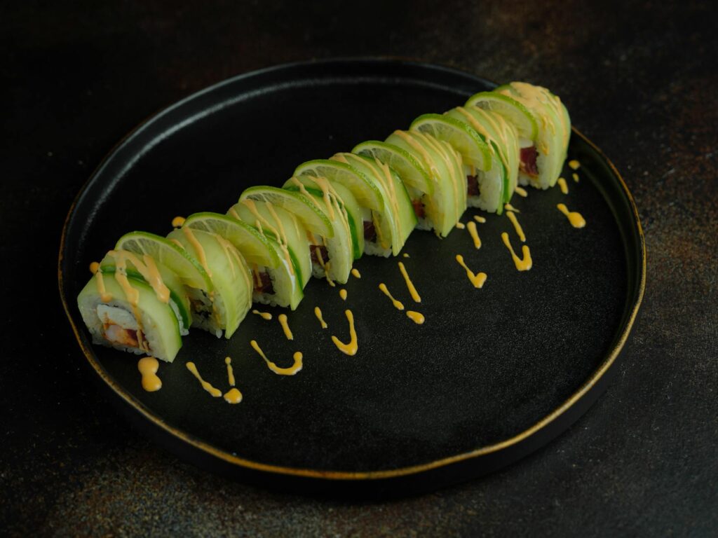 A sushi roll with avocado and sauce on a black plate