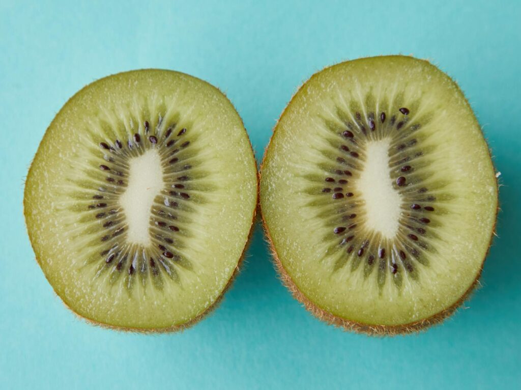 From above of green halves of kiwi with black seeds placed on blue background