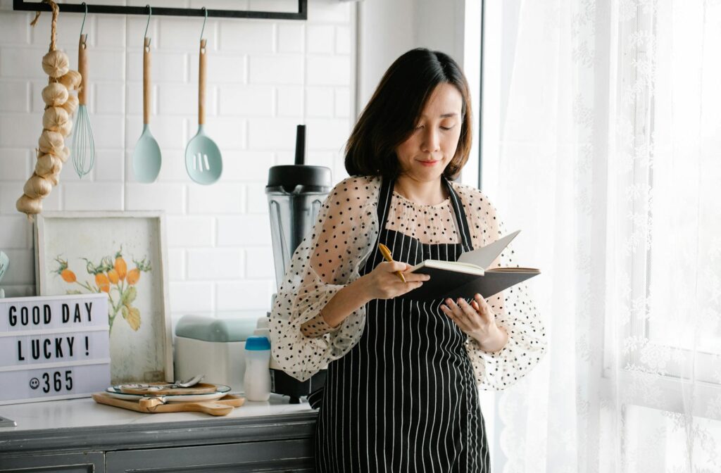 A Woman in an Apron Holding a Journal in a Kitchen