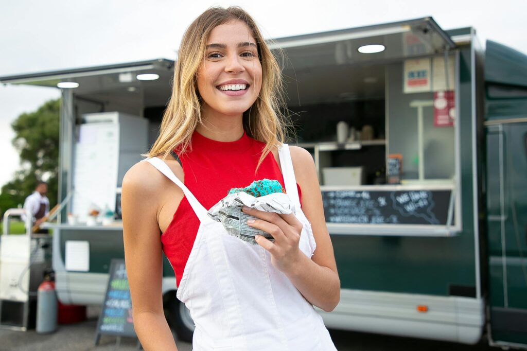 Happy woman standing with burger against food truck