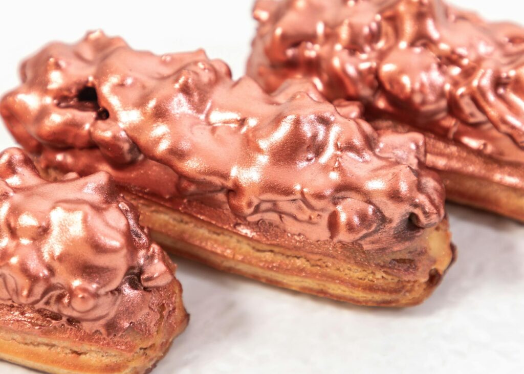 Closeup of served sweet eclair pastries with glaze under golden rose dust on plate