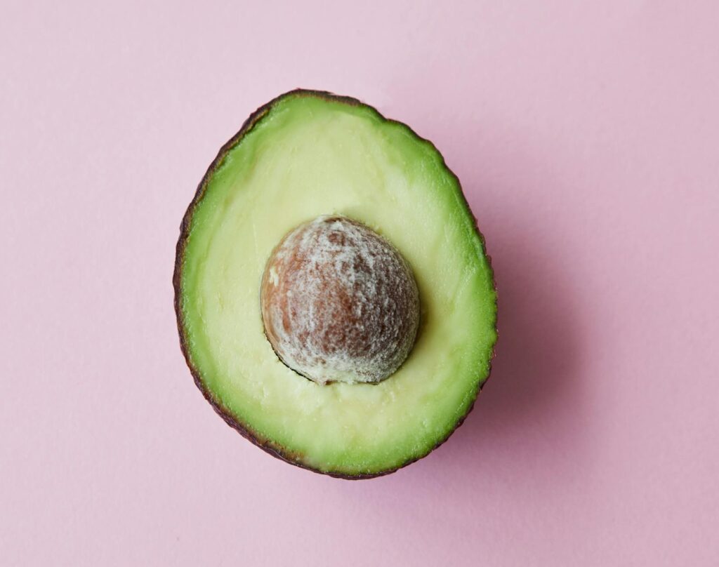 From above of half of fresh raw ripe avocado with seed on purple background