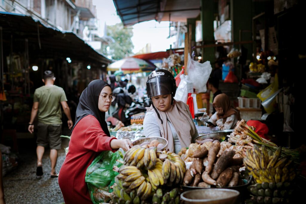 Two women are shopping at a market with bananas